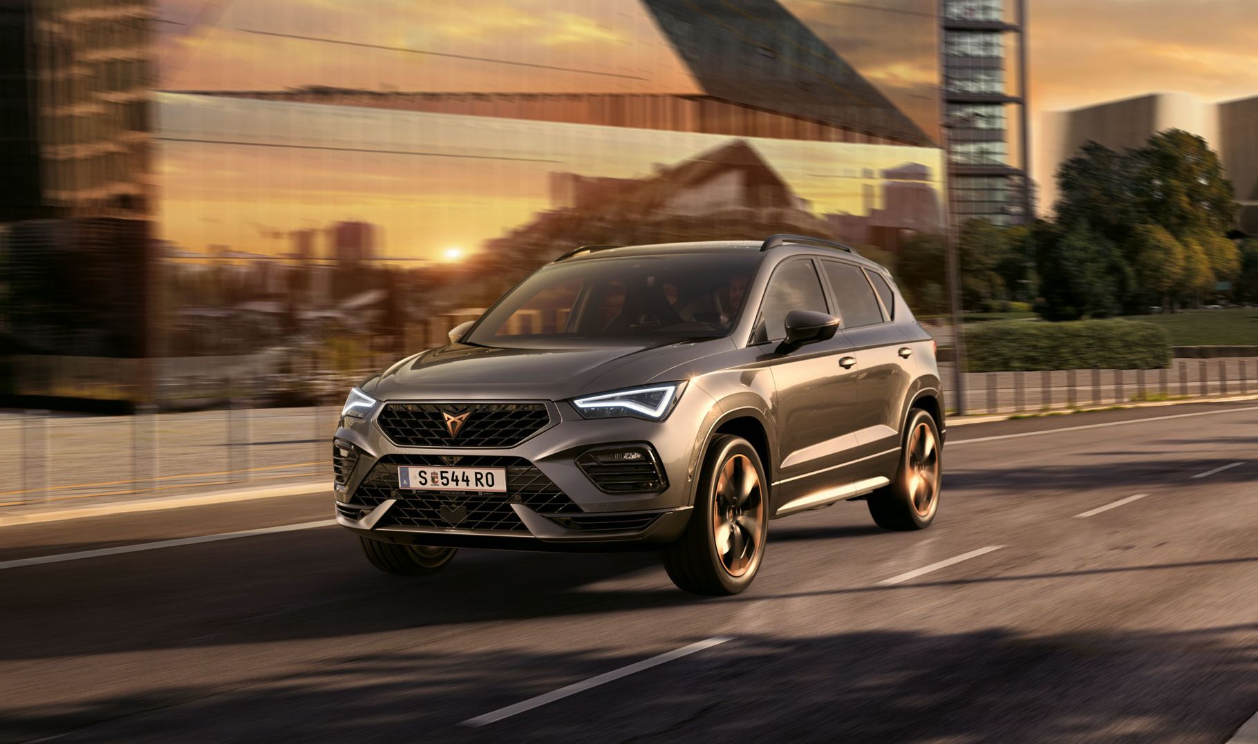 Der CUPRA Ateca SUV fährt bei Sonnenuntergang auf einer Stadtstraße. Der SUV ist mit Motoren mit 150 PS und 190 PS sowie Allradantrieb verfügbar und bietet weniger Emissionen und Kraftstoffverbrauch.