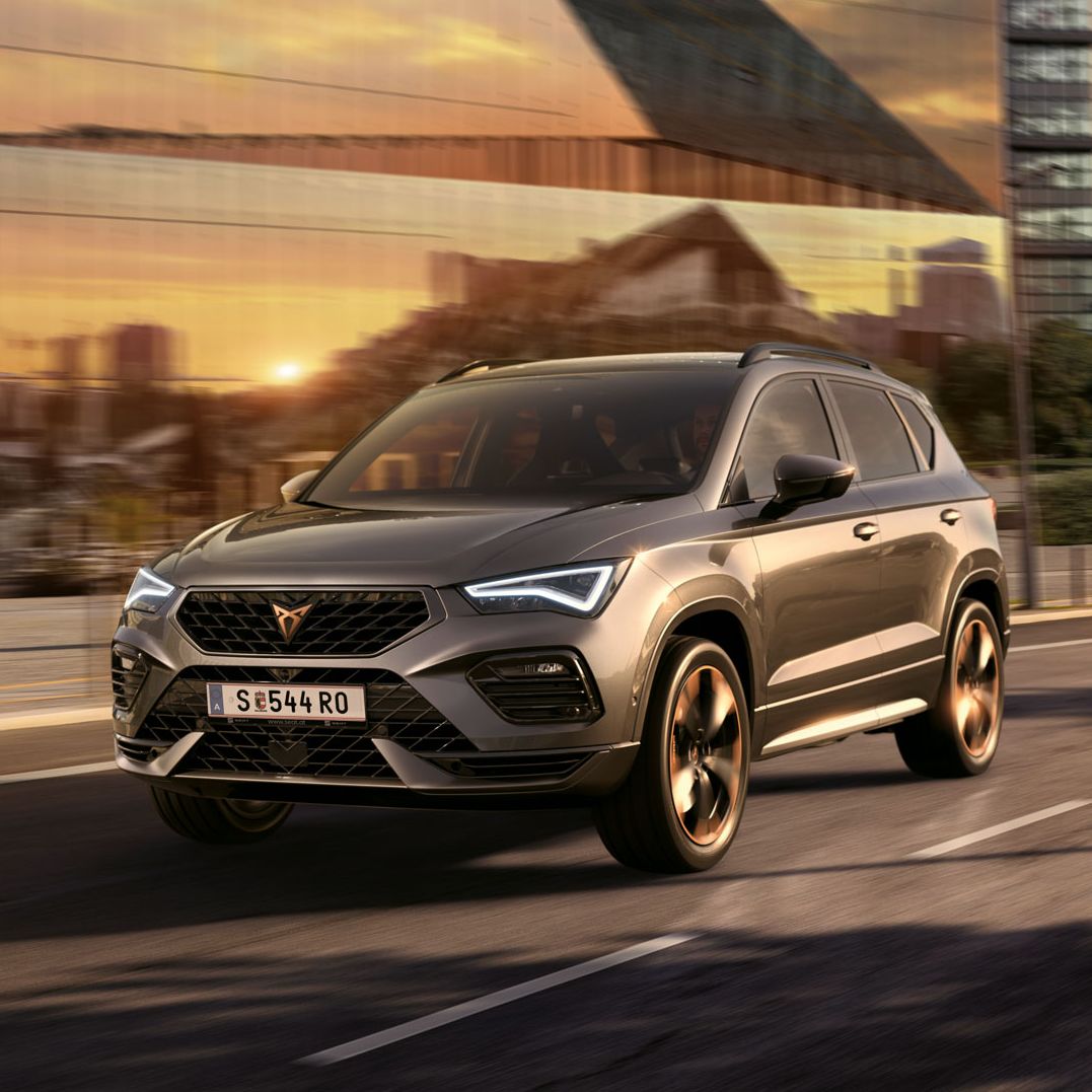 Der CUPRA Ateca SUV fährt bei Sonnenuntergang auf einer Stadtstraße. Der SUV ist mit Motoren mit 150 PS und 190 PS sowie Allradantrieb verfügbar und bietet weniger Emissionen und Kraftstoffverbrauch.