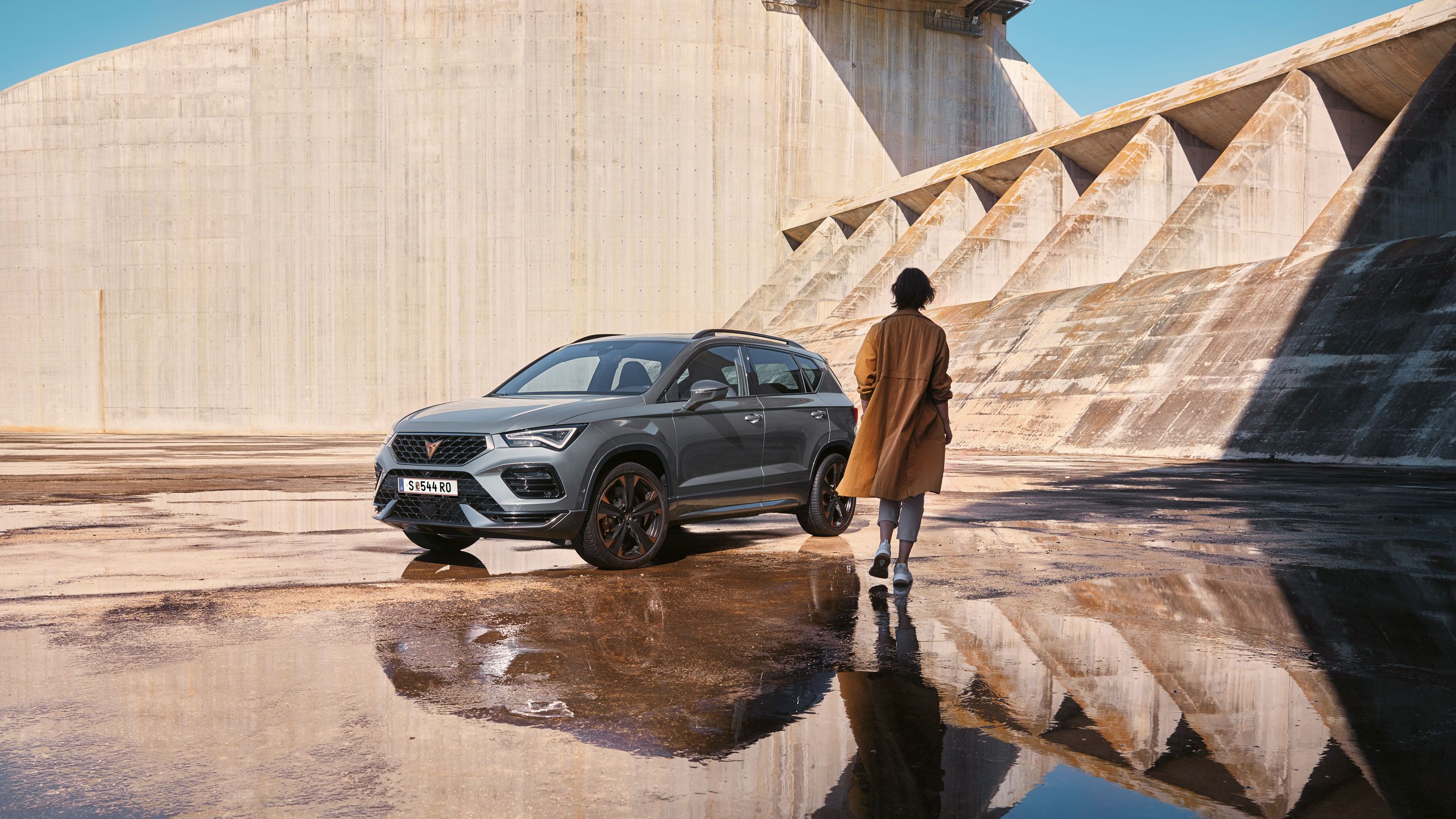 Eine Person geht auf einen CUPRA Ateca zu, der die markanten, athletischen Linien und die dynamische Form zeigt, die den Geist der CUPRA Tribe verkörpern.