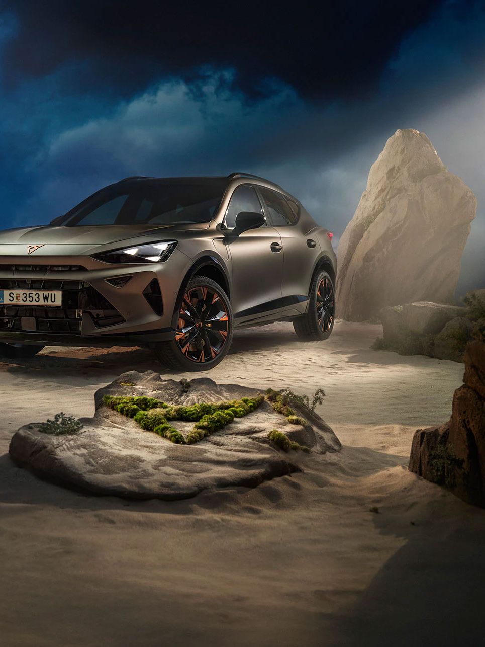 Ein CUPRA Formentor VZ in Bronze steht dramatisch beleuchtet in einer felsigen, nebeligen Landschaft. Eine Lichtstrahl beleuchtet das Fahrzeug und betont seine Konturen. Im Hintergrund sind Felsen und Pflanzen zu sehen.