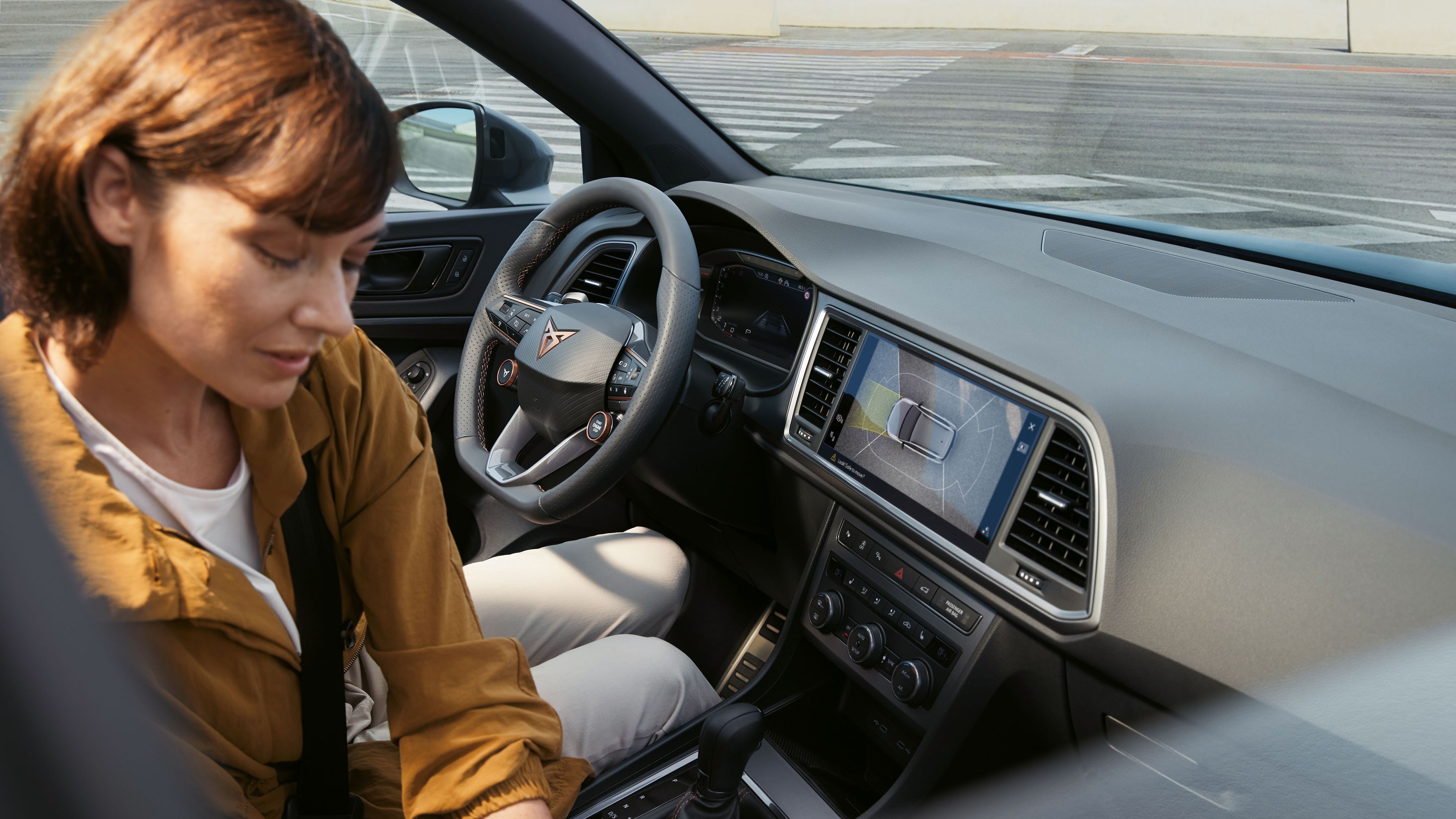 Das Interieur des CUPRA Ateca hebt fortschrittliche Technologiefunktionen hervor. Das Armaturenbrett zeigt einen großen Infotainment-Bildschirm mit Navigation, und das Lenkrad mit Satellitentasten hat integrierte Bedienelemente. Eine Frau sitzt im Inneren.