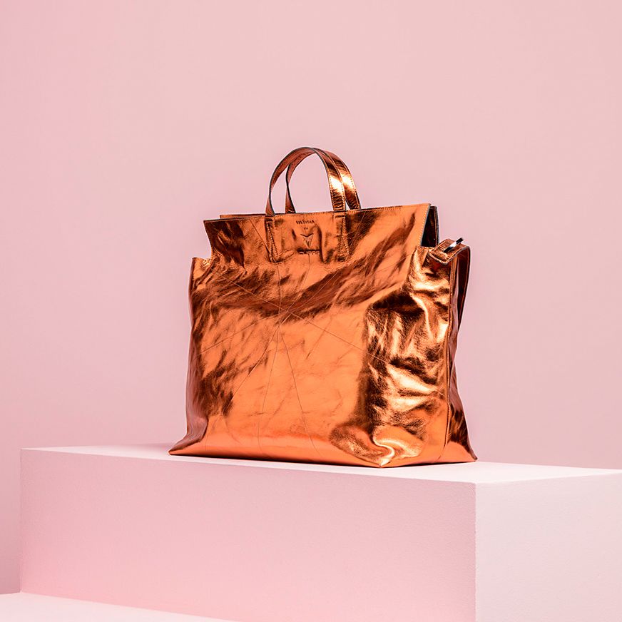 На фото показана сумка металево-мідного кольору на блідо-рожевому фоні